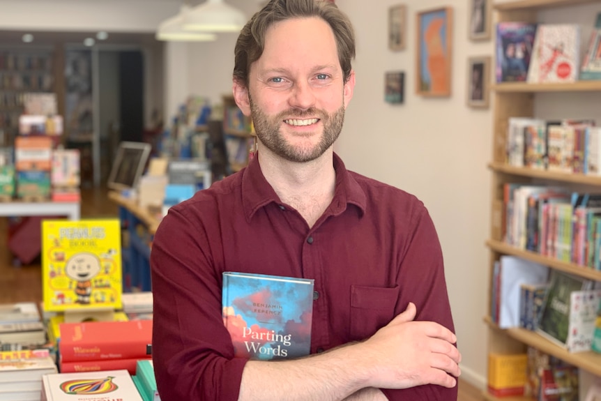 A man holding a book stands in a book shop.