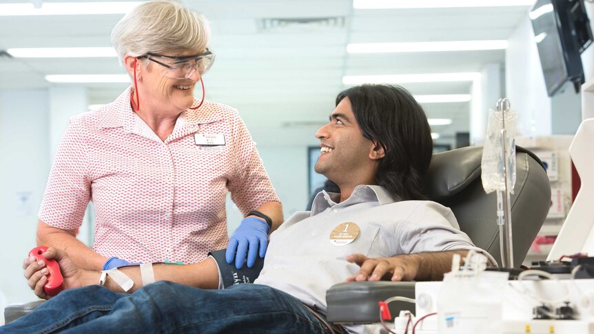 A blood donor sitting in a chair while a Red Cross nurse attends to him.
