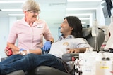 A blood donor sitting in a chair while a Red Cross nurse attends to him.