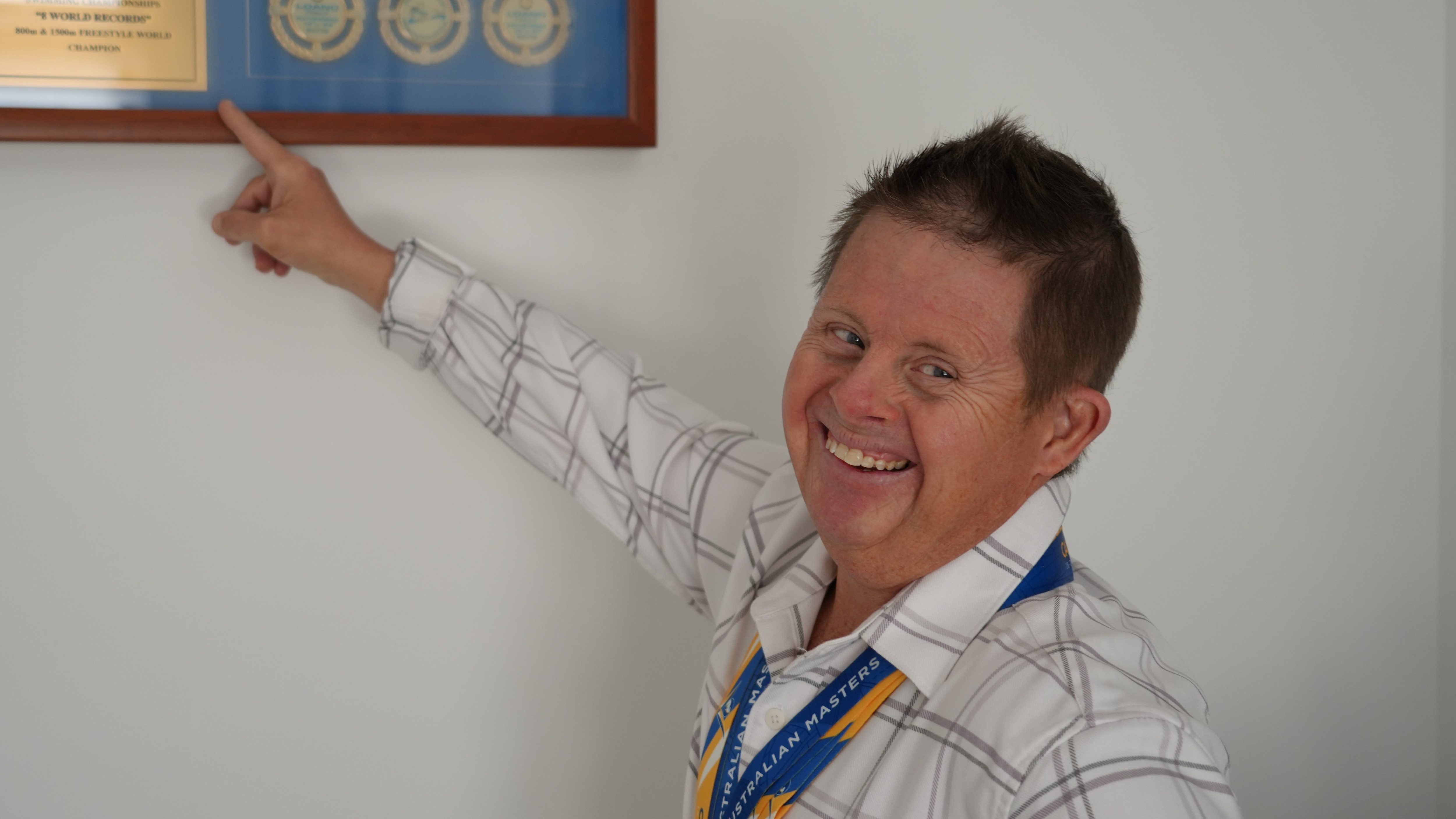 Clinton Stanley smiles and points to a frame hanging on a wall.