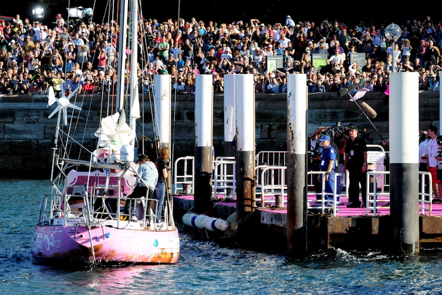 Jessica's pink boat pulls up at a dock while thousands of people watch on.