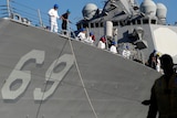 A side view of a grey US warship with the number 69 on side and white clothed sailors on deck