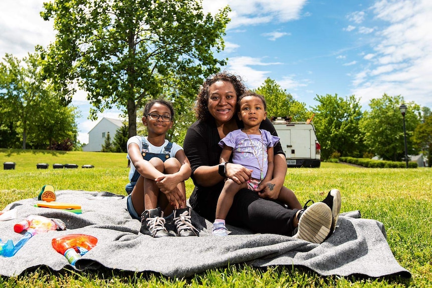 Tina Edwards  sits on a blanket in a park with her two daughters.