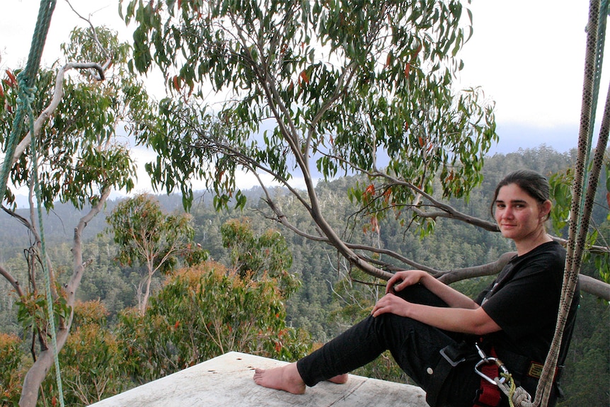 Woman with dark hair is sitting on a small wooden platform above the ground.