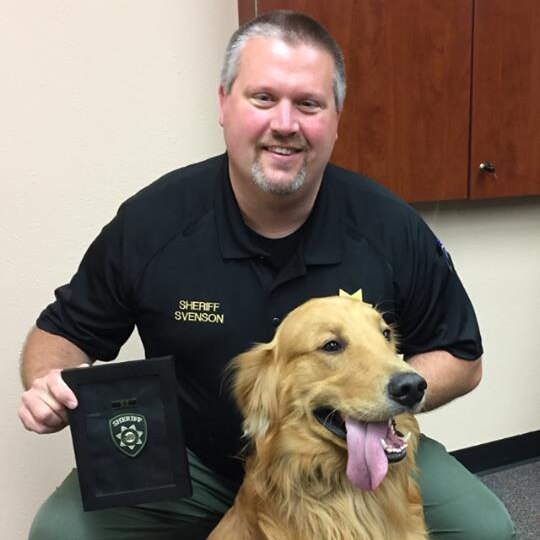 A golden retriever and a police sheriff pose with an official K-9 citation ribbon.