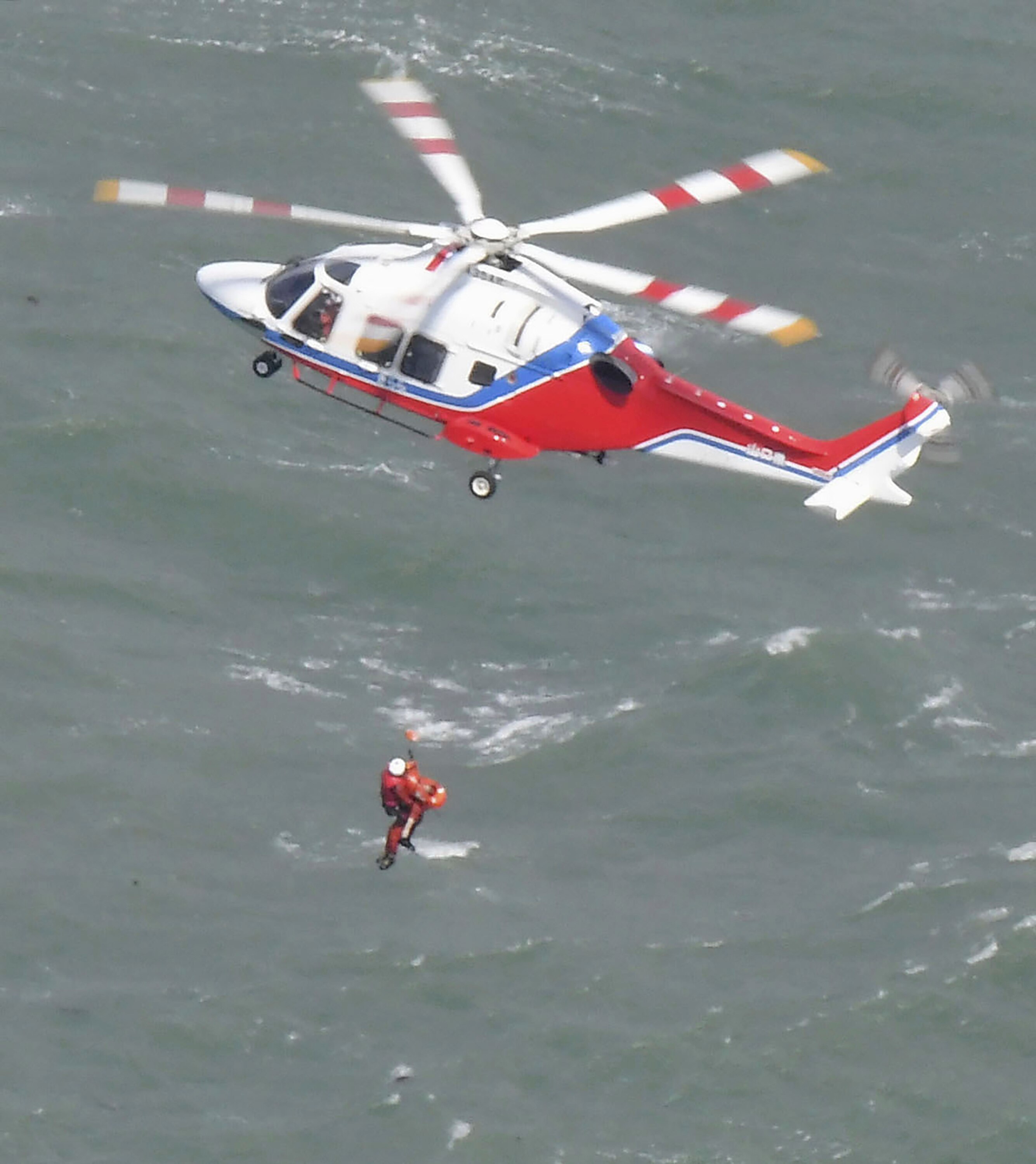 A rescue worker descends from a helicopter above seas