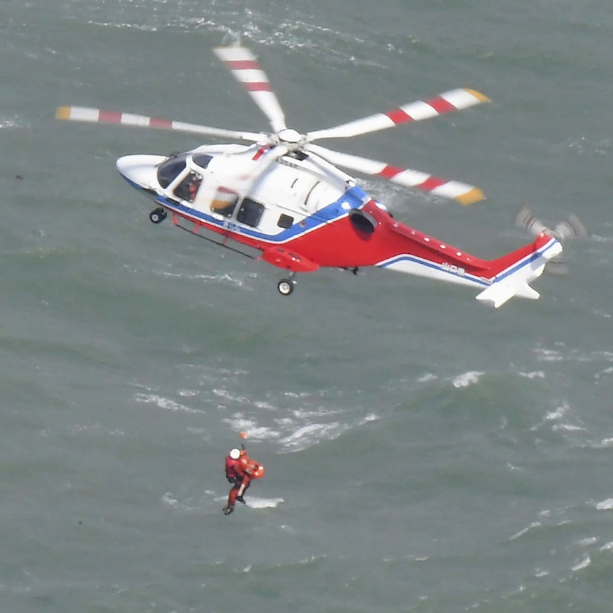 A rescue worker descends from a helicopter above seas