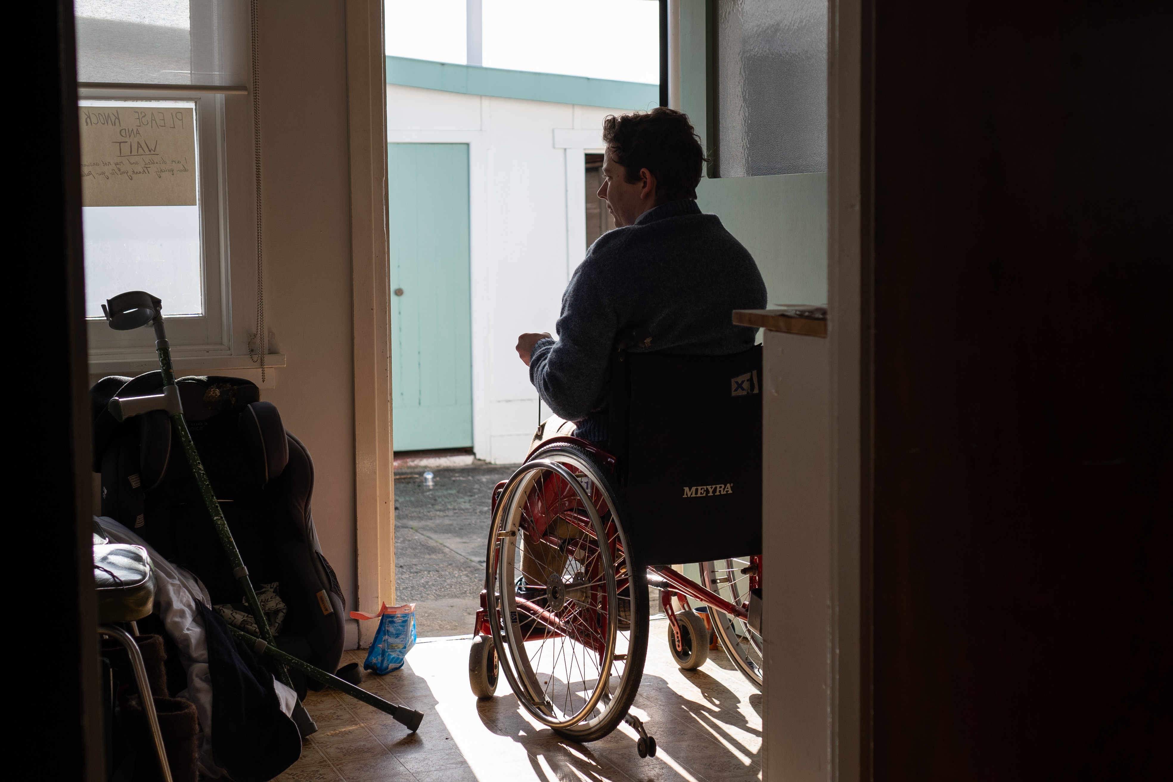 A silhouette of a young man sitting in a wheelchair in a doorway.