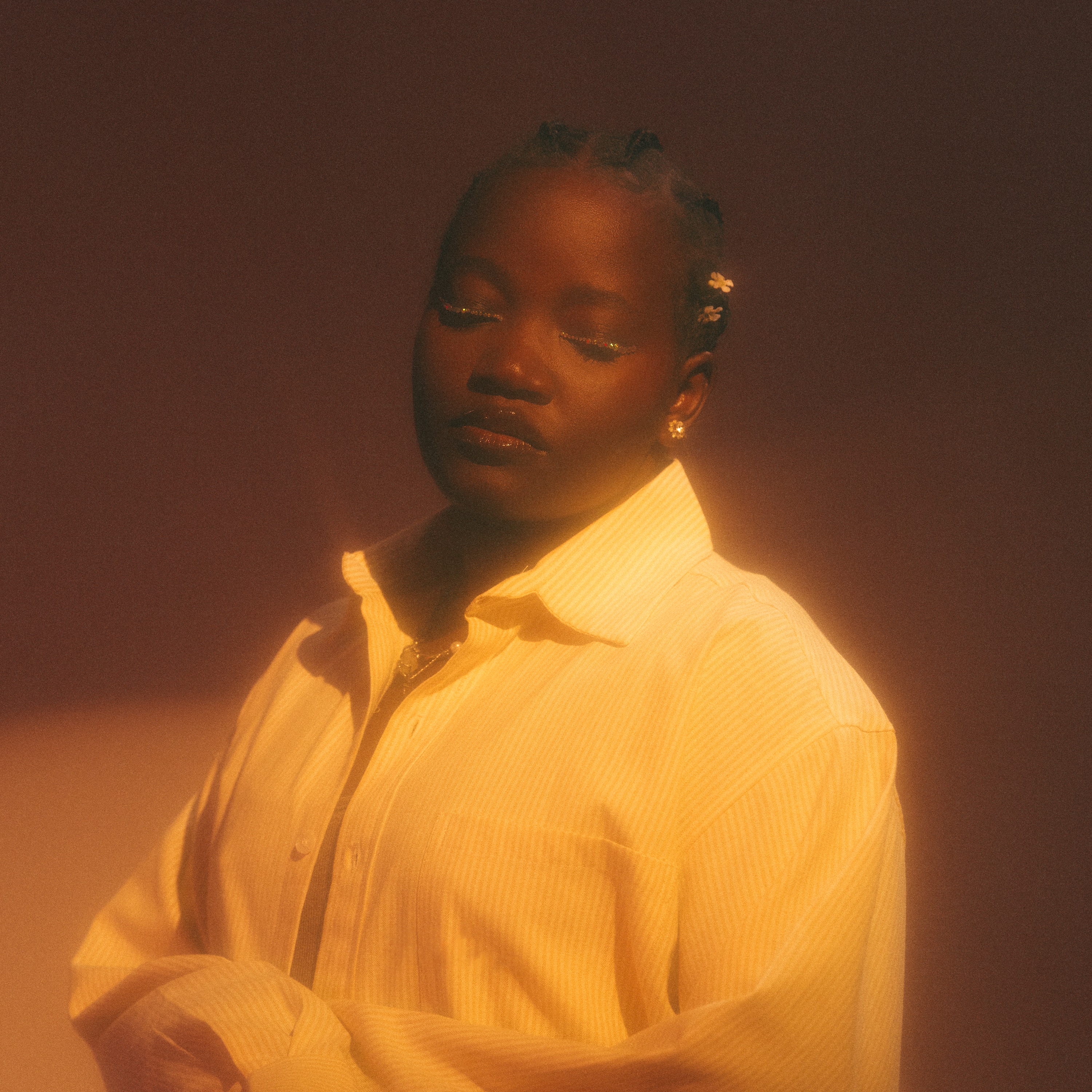 A glossy portrait of musician Beckah Amani, wearing striped collared shirt and braids, eyes closed, against brown backdrop