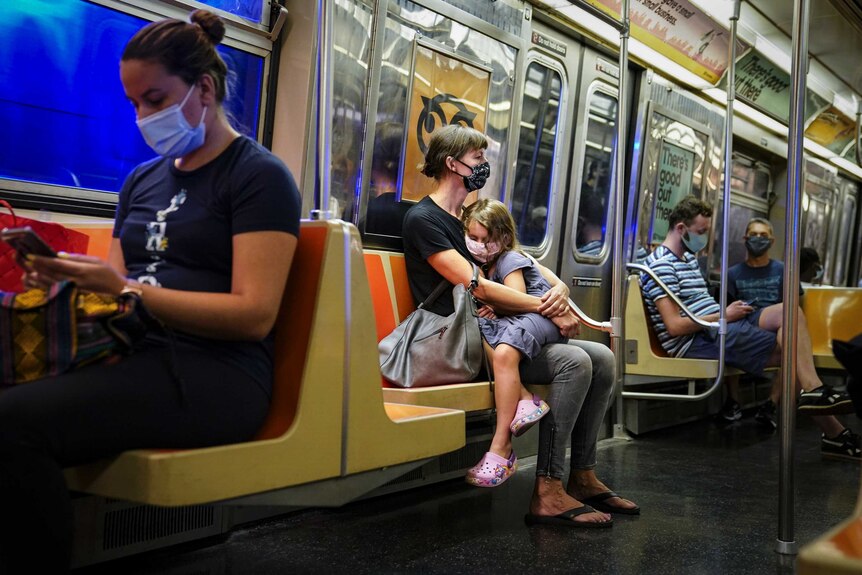 A child rests on a subway car while riders wear protective masks.