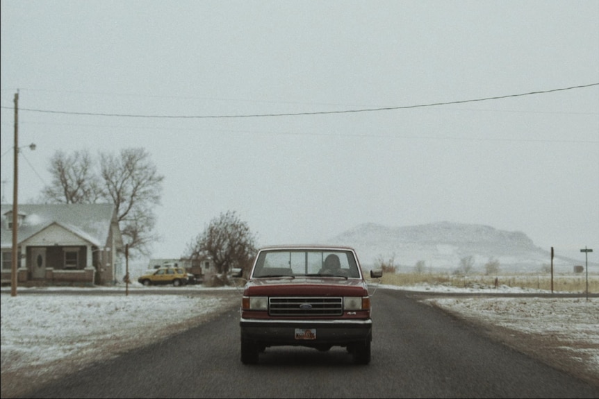 An old pick up truck on a road in a desolate town, snow all around