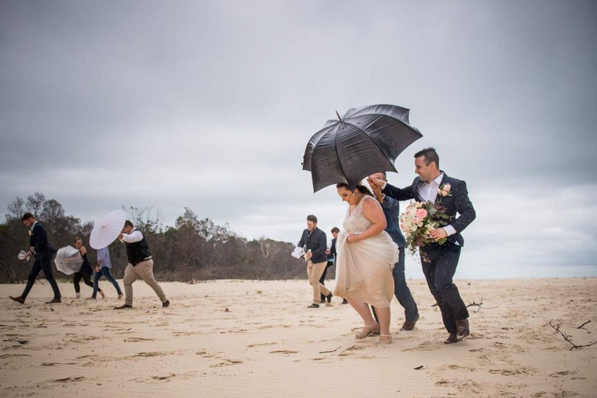 Bride and groom Emma and Danny Gardner run off the beach as rain pours during their wedding photos