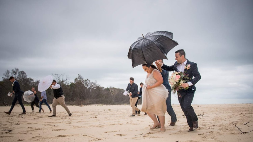 Bride and groom Emma and Danny Gardner run off the beach as rain pours during their wedding photos