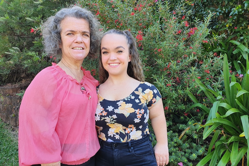 Two short-statured women standing next to each other in front of a bush.