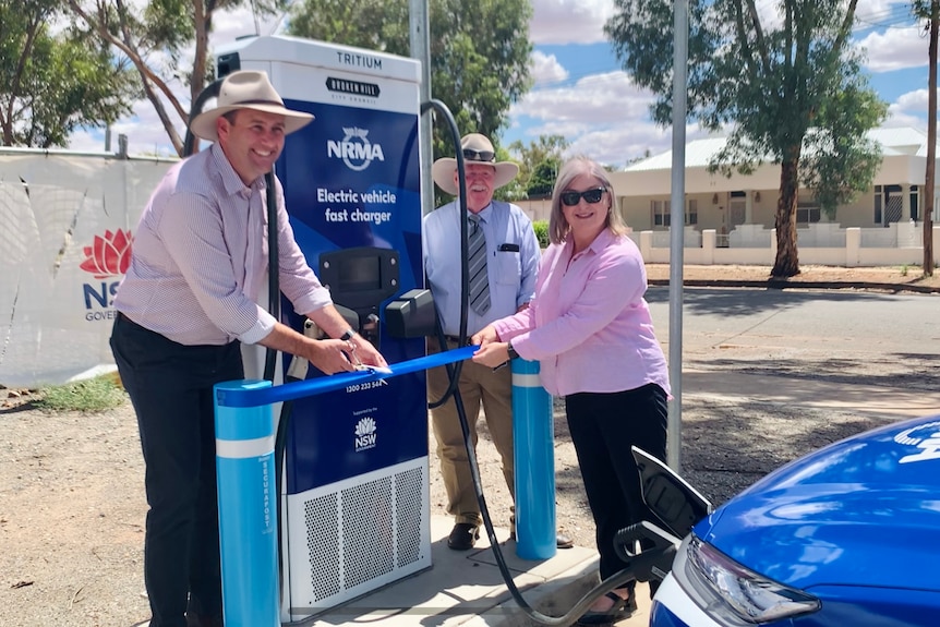Two men and a woman holding a blue ribbon in front of a fast charging station in Broken Hill.
