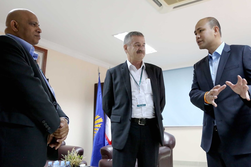 T. Mohan, Alan Parkhouse and Hun Manith stand together in a room talking.