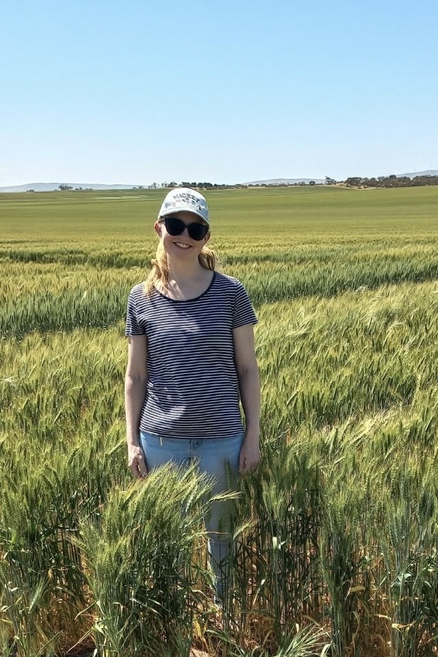 Una mujer sonriente con gorra y camiseta se encuentra en un campo de trigo.