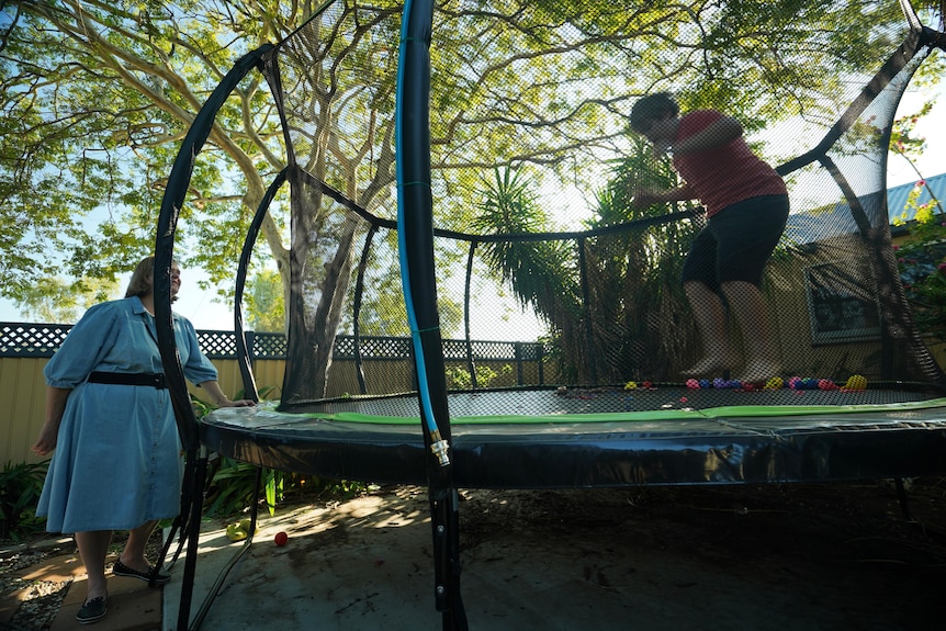 A mother watches her 11-year-old son jump on a trampoline.