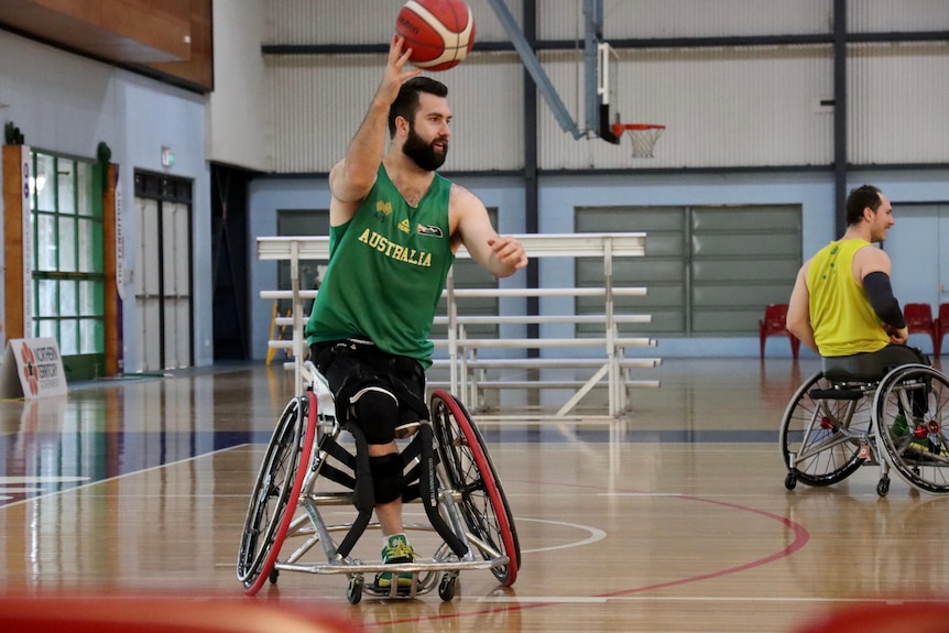 A young man in a wheelchair wearing green and gold plays basketball.