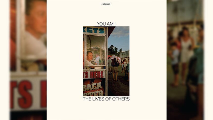 a woman sits in a ticket booth at a carnival on the cover of you am i's album the lives of others