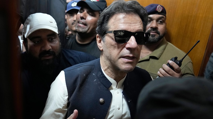 Imran Khan walks through a dense crowd of men as he tries to leave a courtroom while wearing sunglasses.