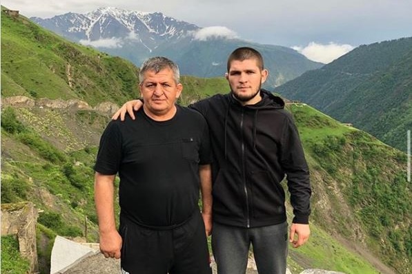 A MMA fighter stands next to his father, as they stand with mountains in the background.