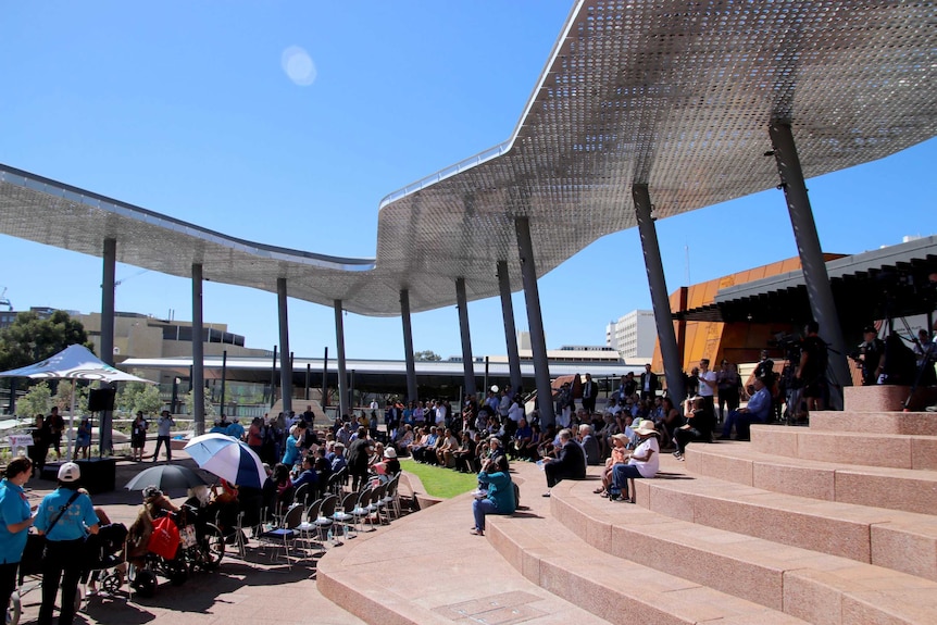 People sitting on tiered steps under an angular silver metal shade.