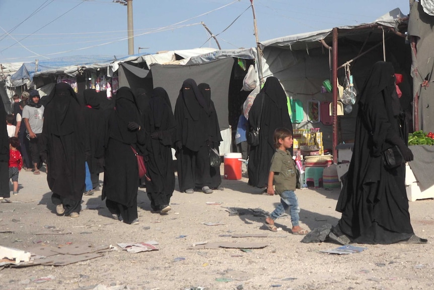 Child in Syrian refugee camp walks among women in black billowing robes.