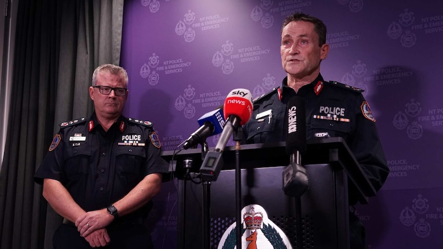 Two men in police uniform in front of a purple branded NT police banner