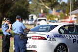 Two police officers stand at the rear of a police car with paperwork.