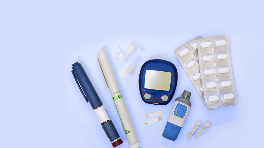 Diabetic kit: glucometer, test strips, lancet, metformin tablets. Top view, blue background, empty space
