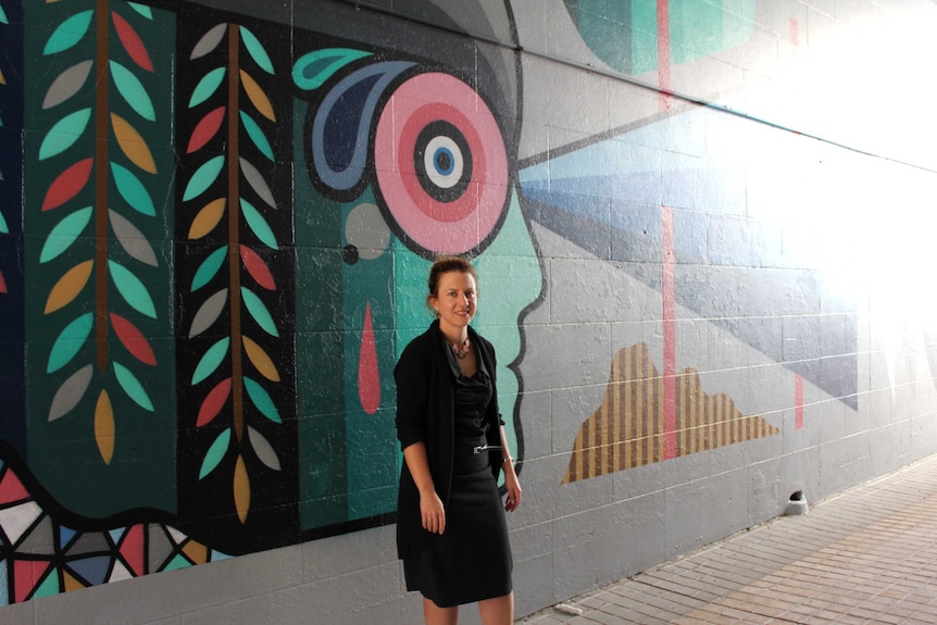 A lady stands in front of a vibrant mural in an alleyway off Adelaide Street Maryborough