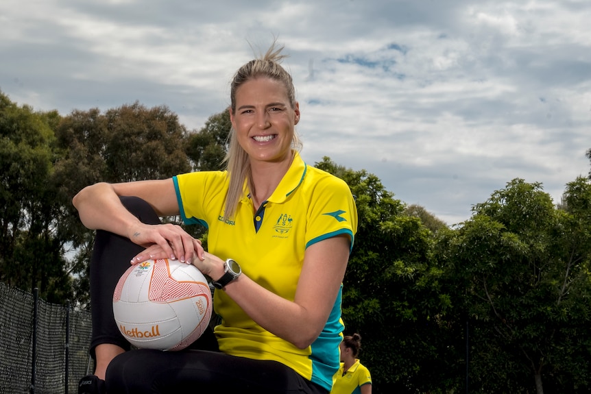 Caitlin Bassett sits, resting her arms and the ball against her right knee which is raised. 