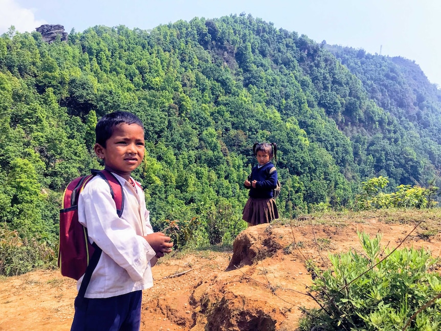 Two small Nepalese children carrying backpacks in front of the Himalaya mountains.