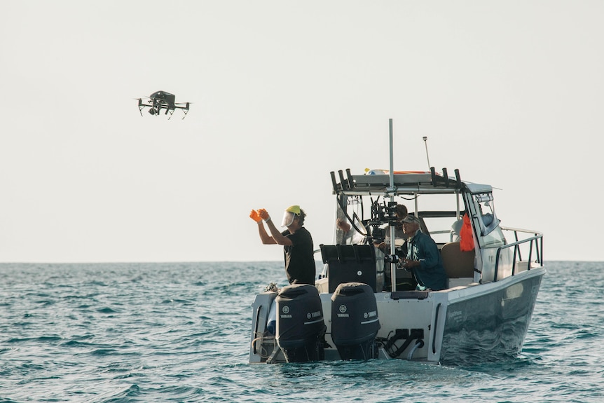 Man operating a drone at sea from the back of a boat while other crew watch on.