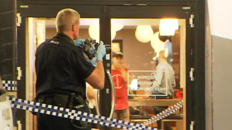 A police officer taking a photograph of a glass door with crime tape behind him