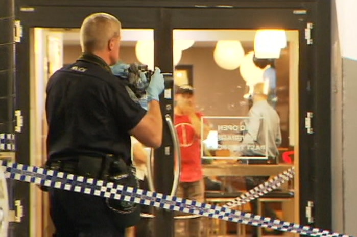 A police officer taking a photograph of a glass door with crime tape behind him