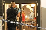 A police officer taking a photograph of a glass door with crime tape behind him
