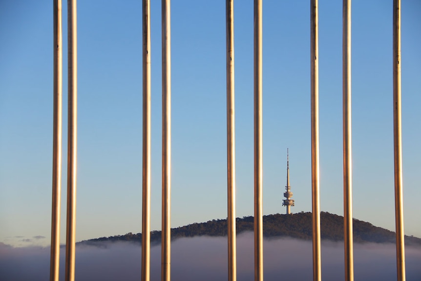 Telstra Tower above fog seen through the flagpoles