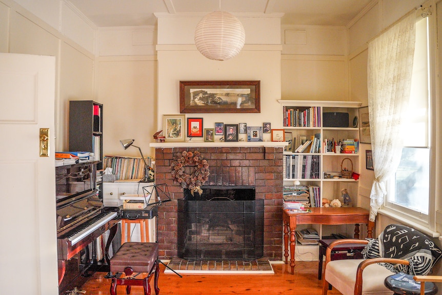 An old brick fireplace in a living room surrounded by bookshelves and a piano.