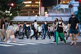 A crowded street crossing in Tokyo, with most pedestrians in masks. 