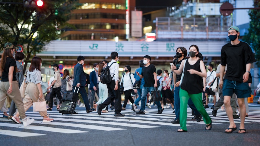 A crowded street crossing in Tokyo, with most pedestrians in masks. 