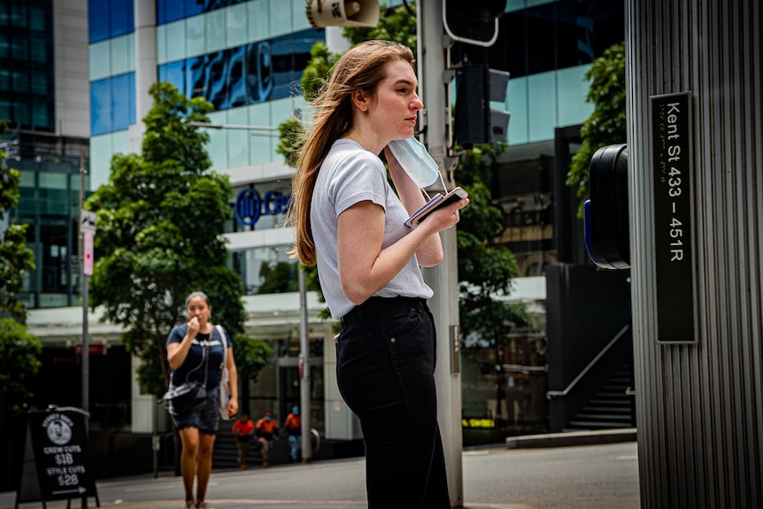 A woman stands at a passenger crossing holdings a face mask.