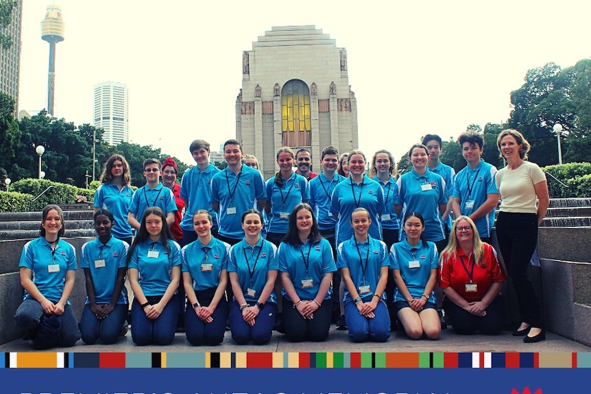 Twenty students wearing a blue uniform stand in front of Sydney's Anzac Memorial.