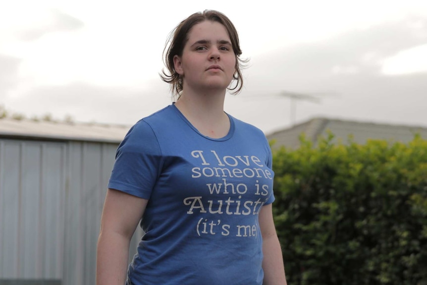 Maria Scharnke is standing with her chin raised, wearing a t-shirt saying "I love someone who is autistic. It's me".