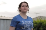 Maria Scharnke is standing with her chin raised, wearing a t-shirt saying "I love someone who is autistic. It's me".