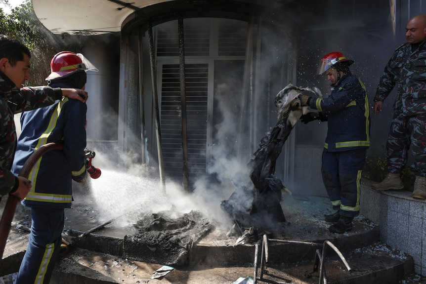 Firefighter spraying water at a building, a second lifting debris