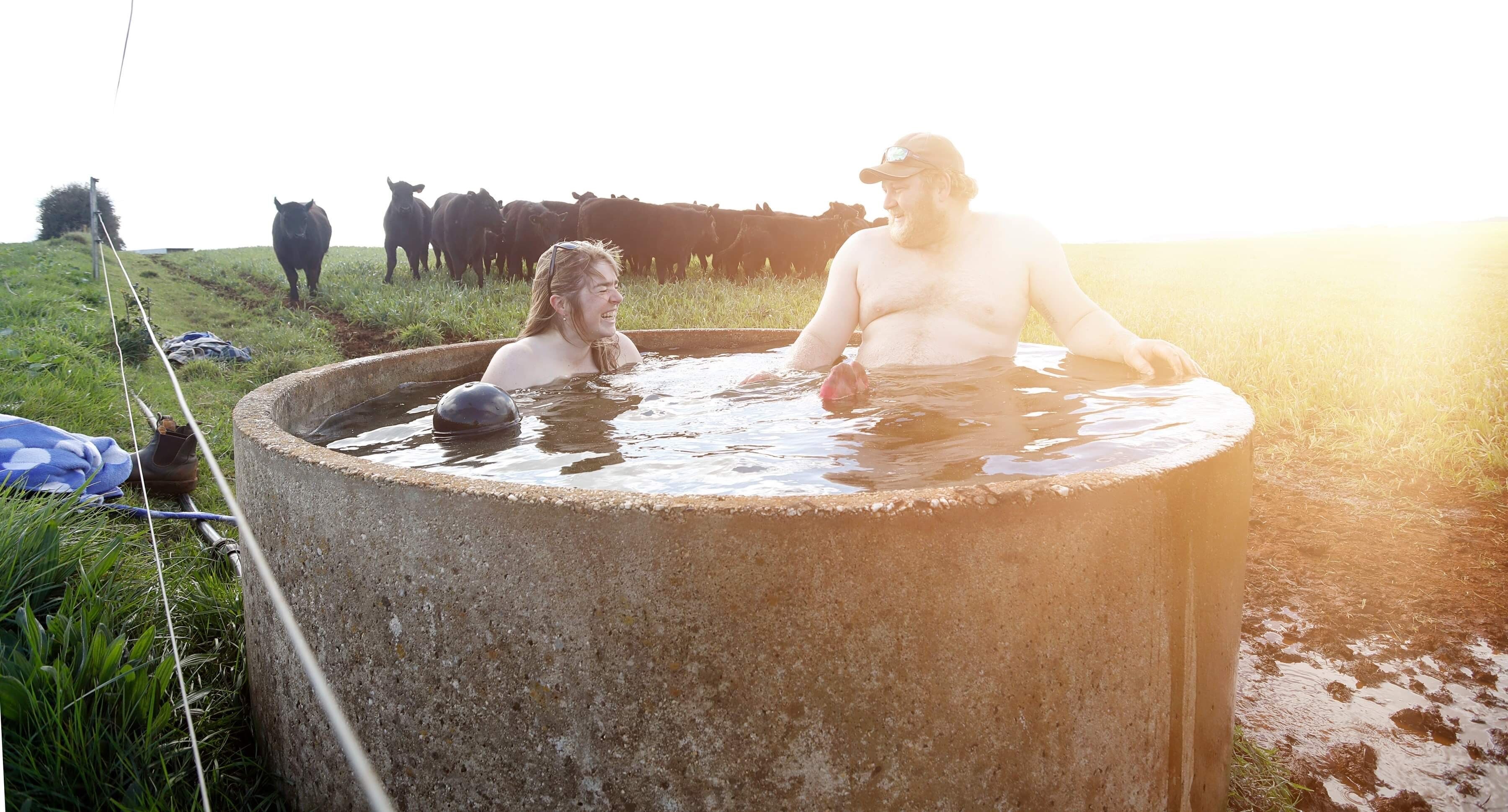 A man and woman ease into the cool water of a small cattle watering reservoir