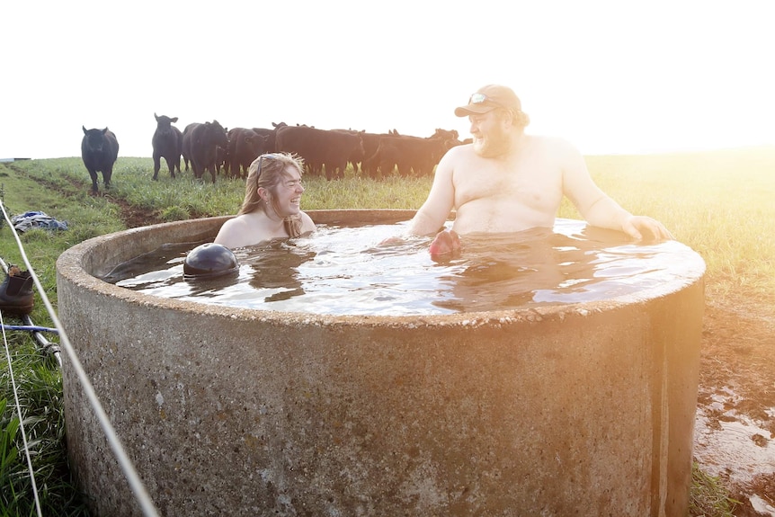 A man and woman ease into the cool water of a small cattle watering reservoir