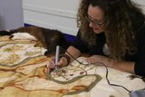 A woman works on a possum skin cloak.